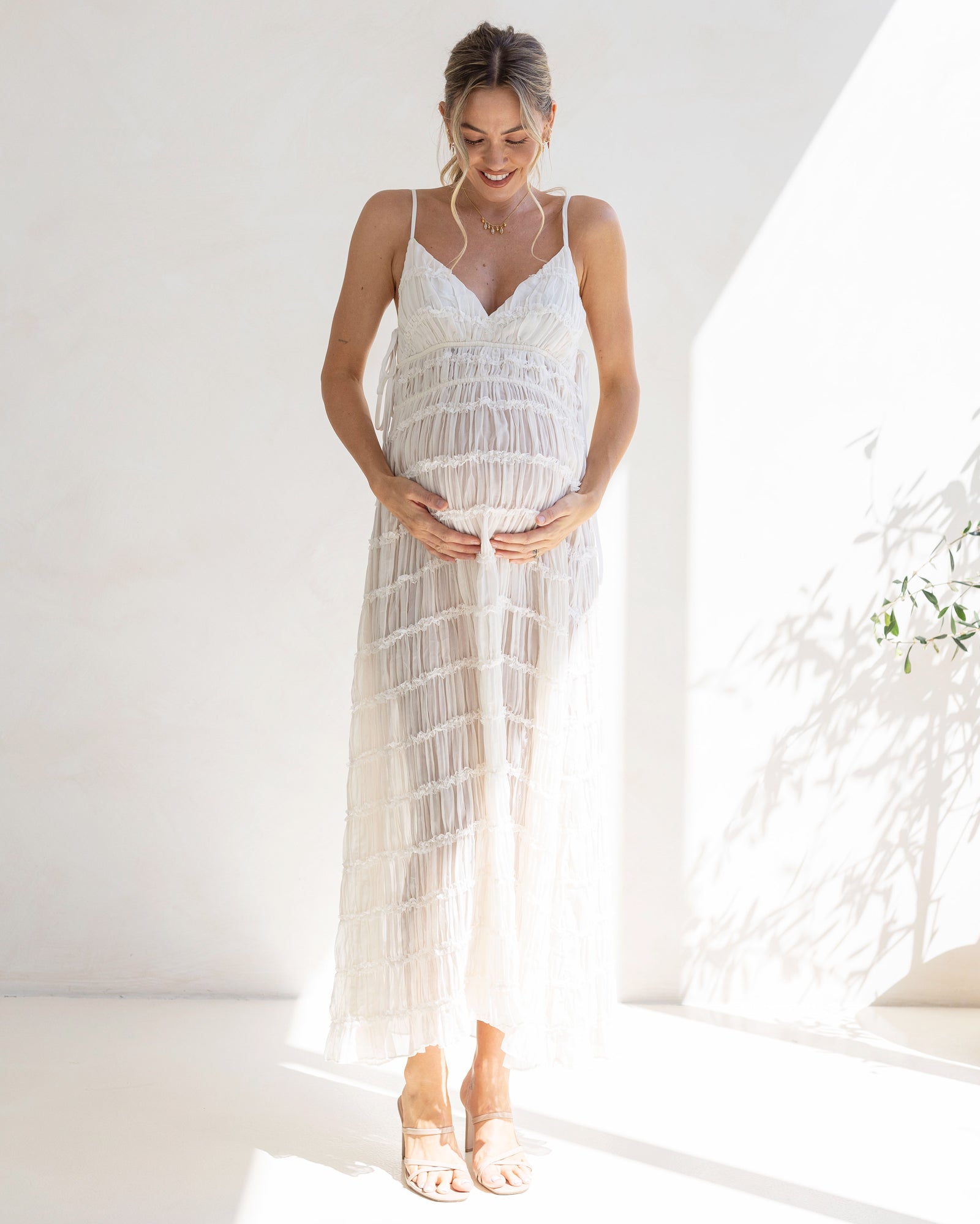 Woman wearing a white lace maternity dress standing in a bright room.