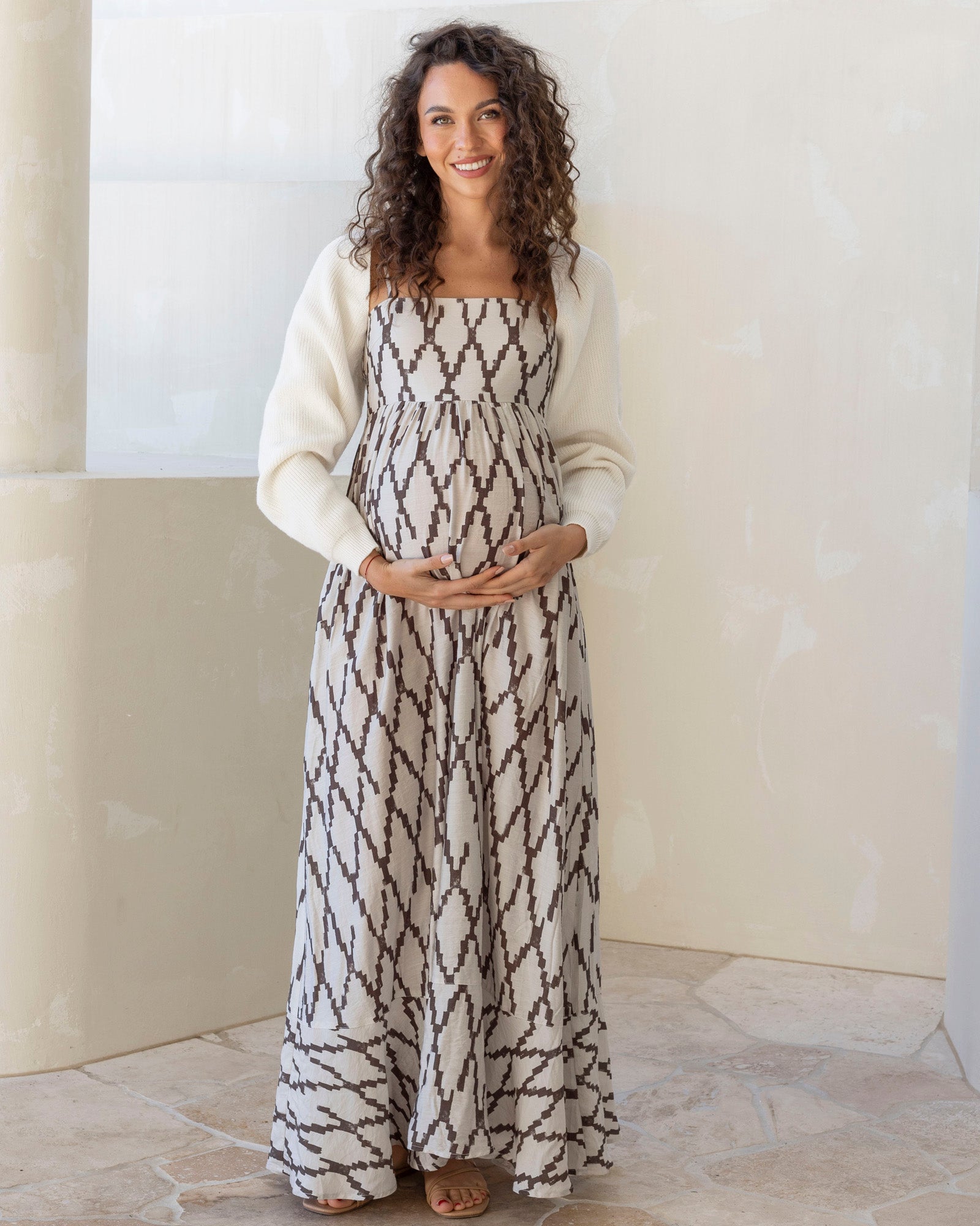 Woman wearing a long, patterned dress with a white cardigan against a neutral background