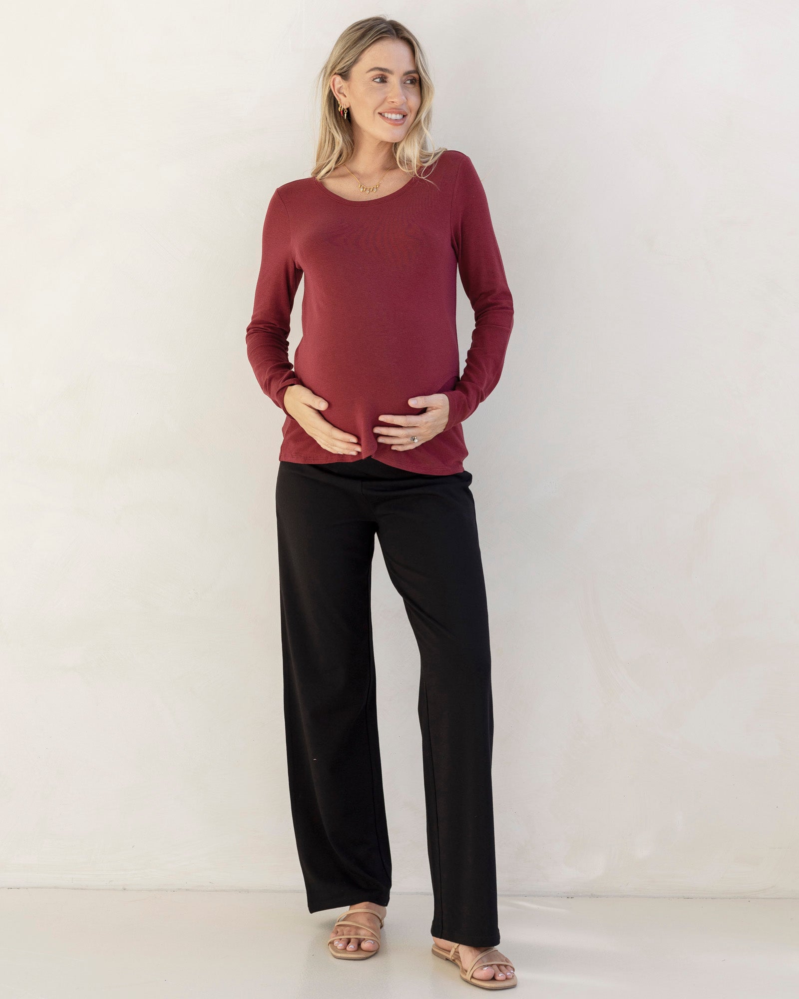 Woman wearing a burgundy long-sleeve top and black pants against a white background