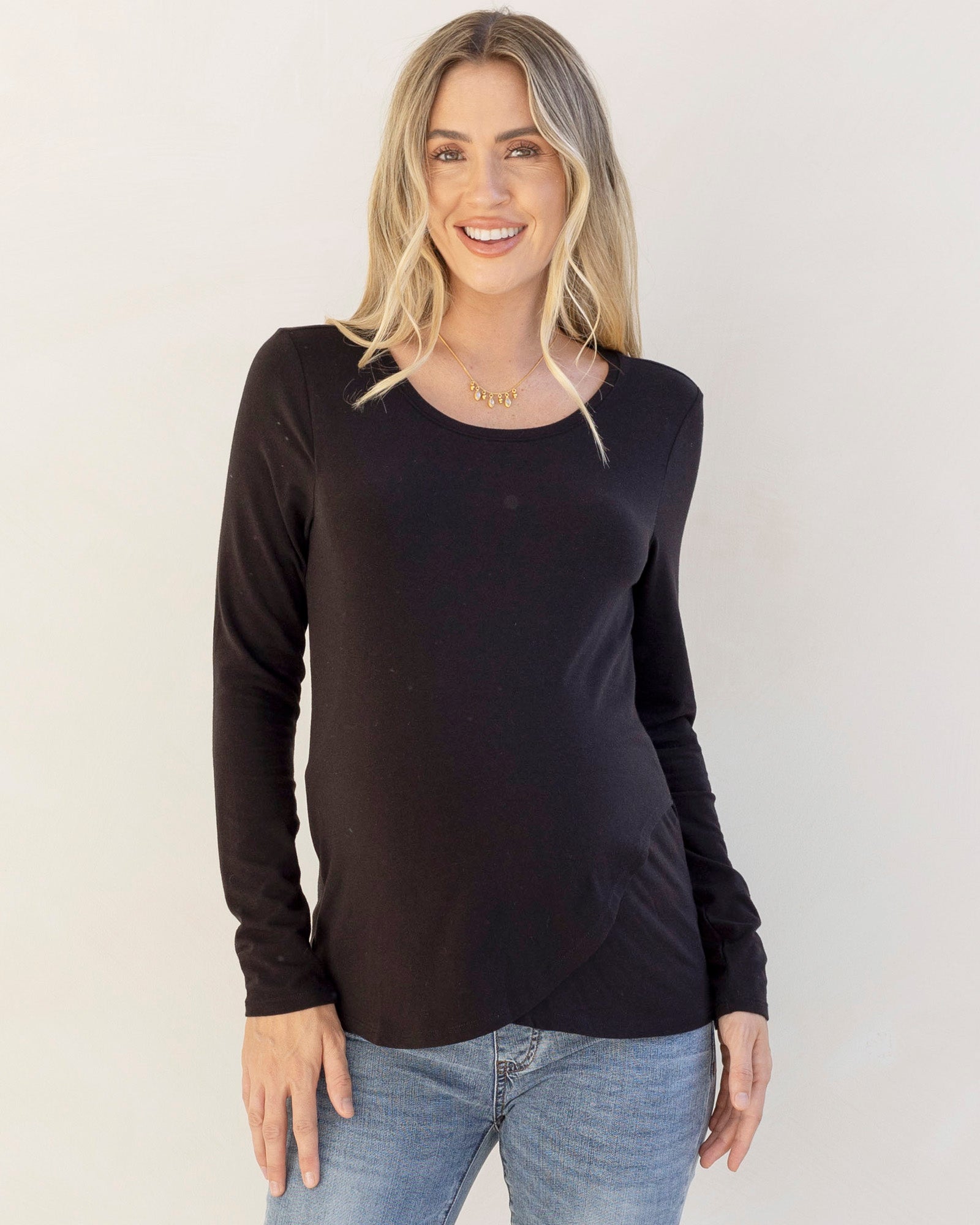 Woman wearing a black long-sleeve nursing top and blue jeans against a plain background