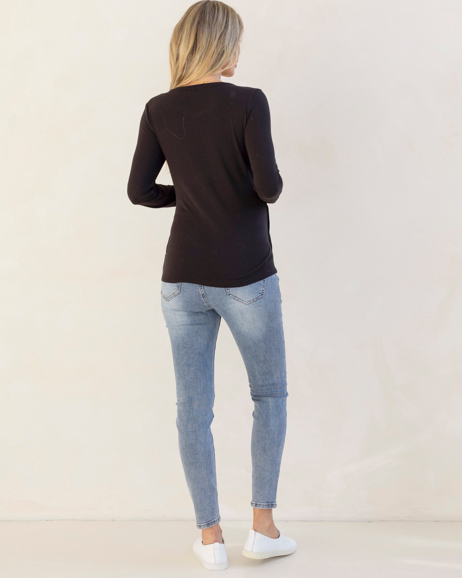 Person wearing a black long-sleeve top and light blue jeans on a plain background