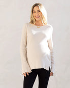 A woman wearing a cream-colored oversized maternity and nursing jumper with long bell sleeves and side button opening for breastfeeding.