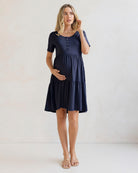 A pregnant woman wearing a navy maternity button front dress with short sleeves and a knee-length design.