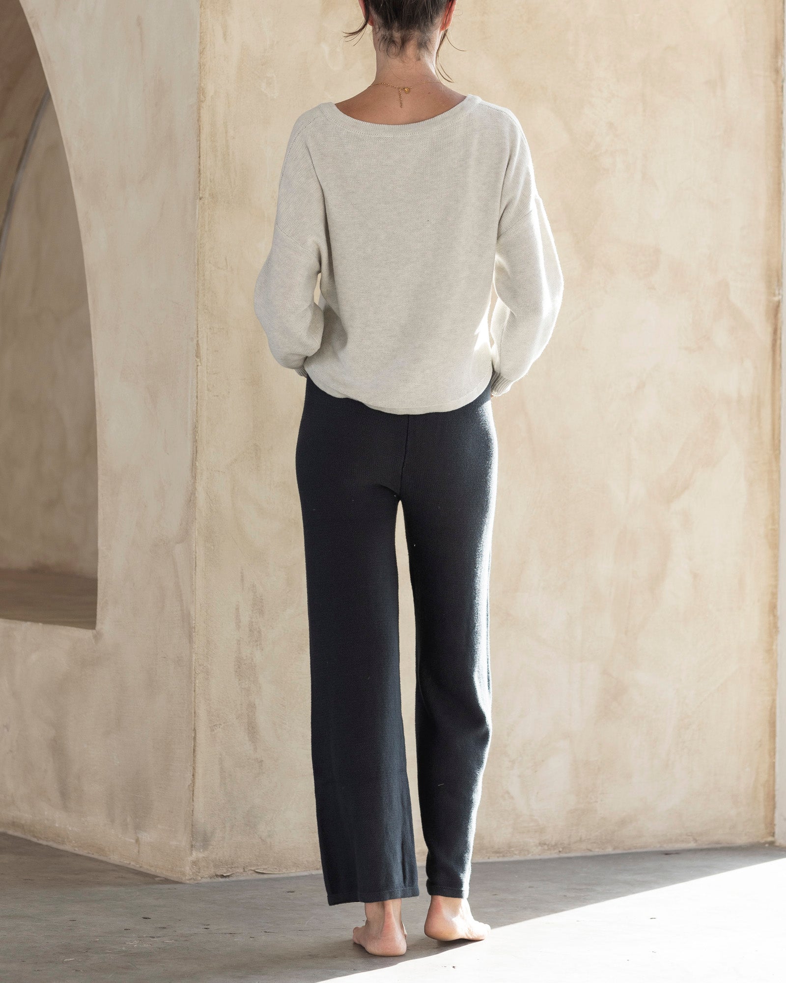 Person wearing a light gray sweater and dark pants in a neutral setting
