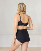 Woman wearing a black bra and high-waisted underwear against a neutral background