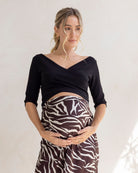 Pregnant woman wearing a black maternity top and zebra print skirt against a plain background