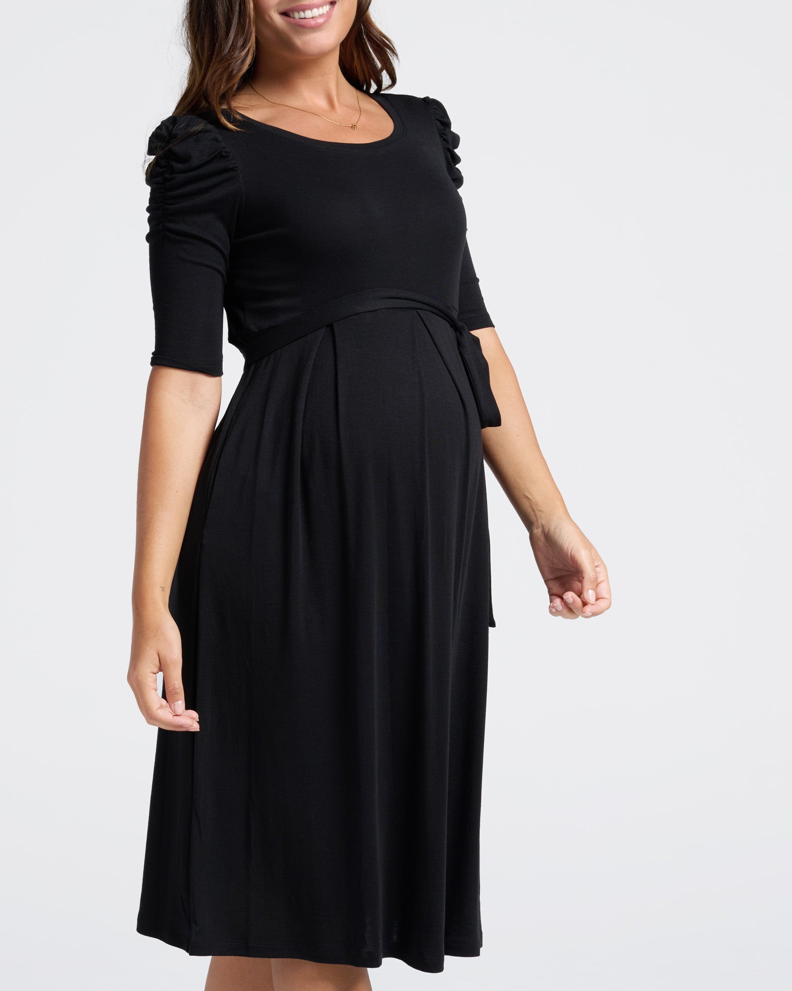 Woman wearing a black maternity work dress with puff sleeves on a white background