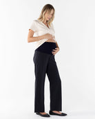 A pregnant woman wearing black relaxed fit maternity pants with an adjustable waistband and a white top.