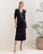 Woman wearing a black maternity knit dress with white buttons in a minimalistic setting