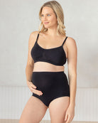 Woman wearing a black maternity bra and high-waisted underwear against a plain background