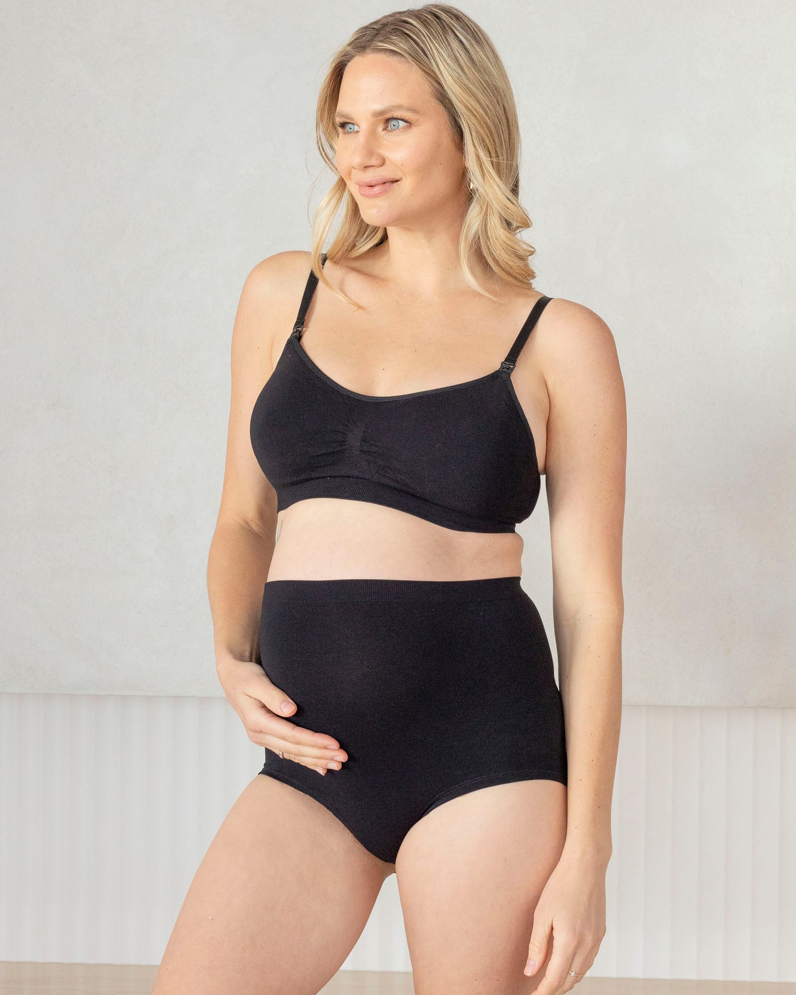 Woman wearing a black maternity bra and high-waisted underwear against a plain background