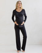 A pregnant woman wearing a black 2-piece maternity sleepwear set with a button-down top and high-waisted pants.