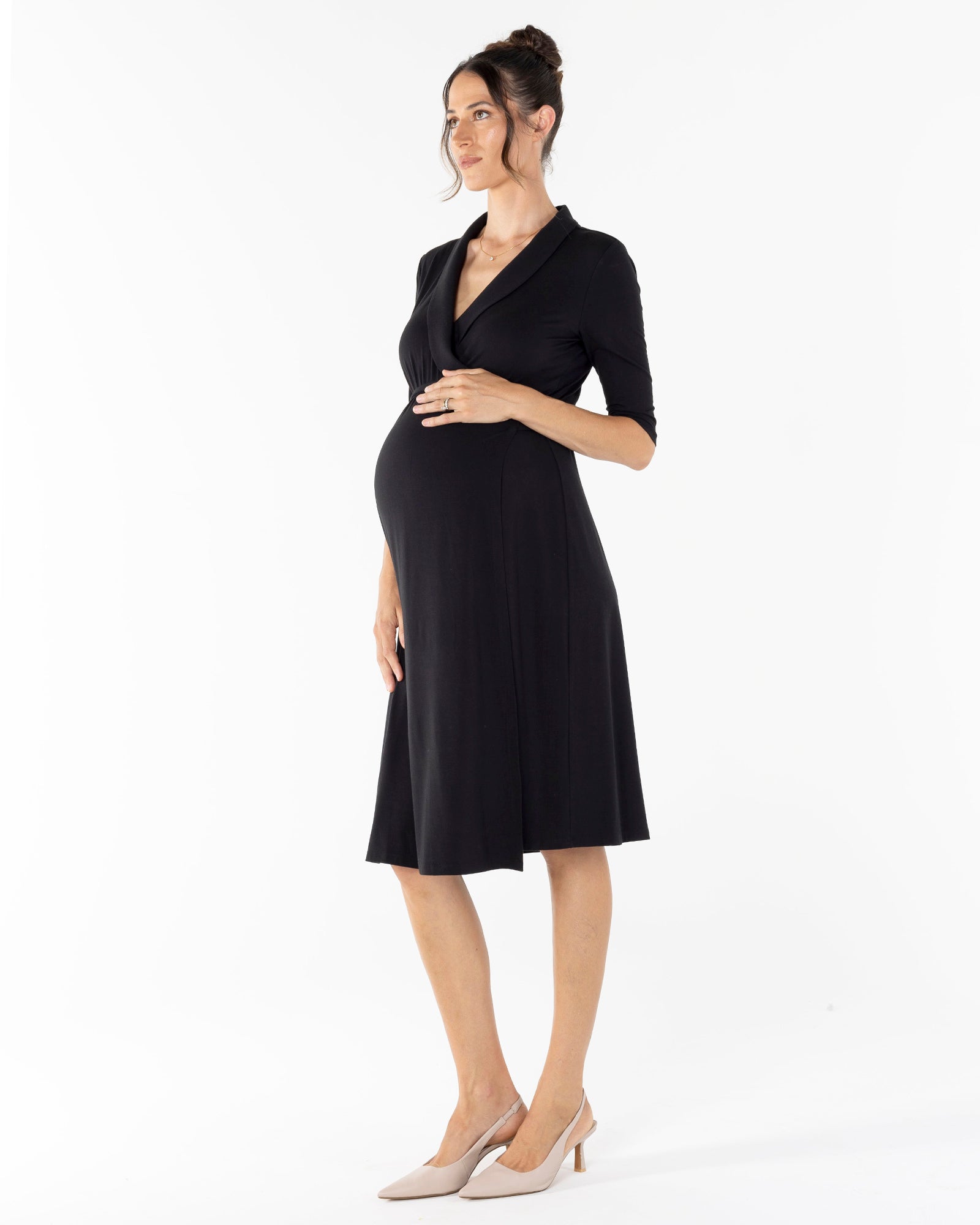 A pregnant woman wearing a black maternity wrap dress with a wide neckline and short sleeves.
