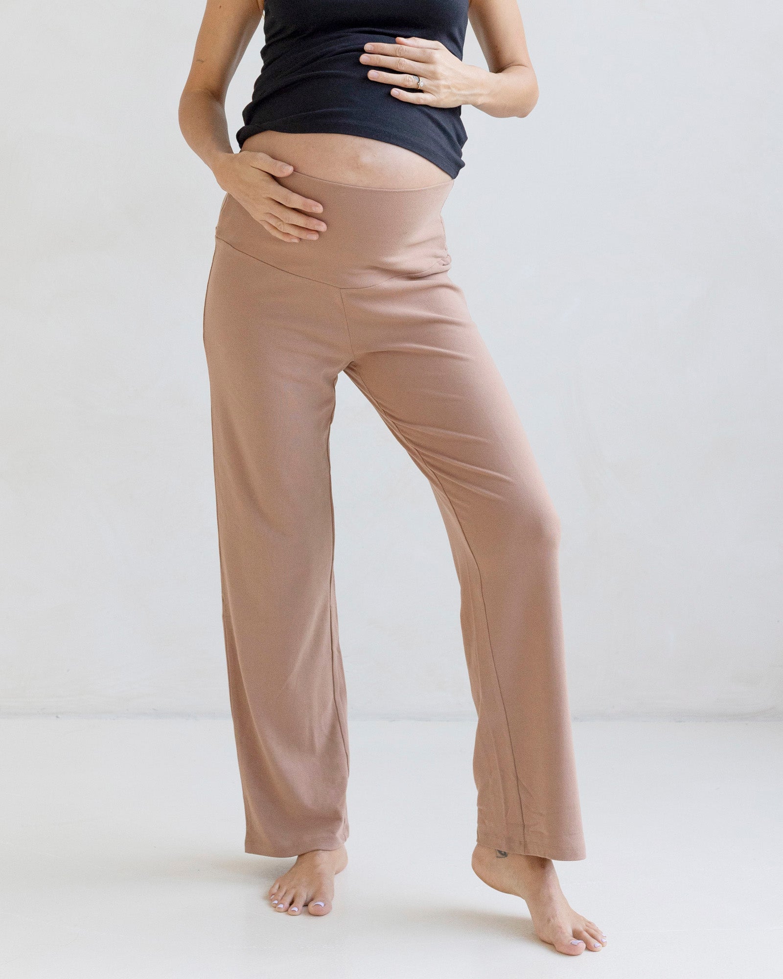 Person wearing beige maternity pants and a black top on a white background