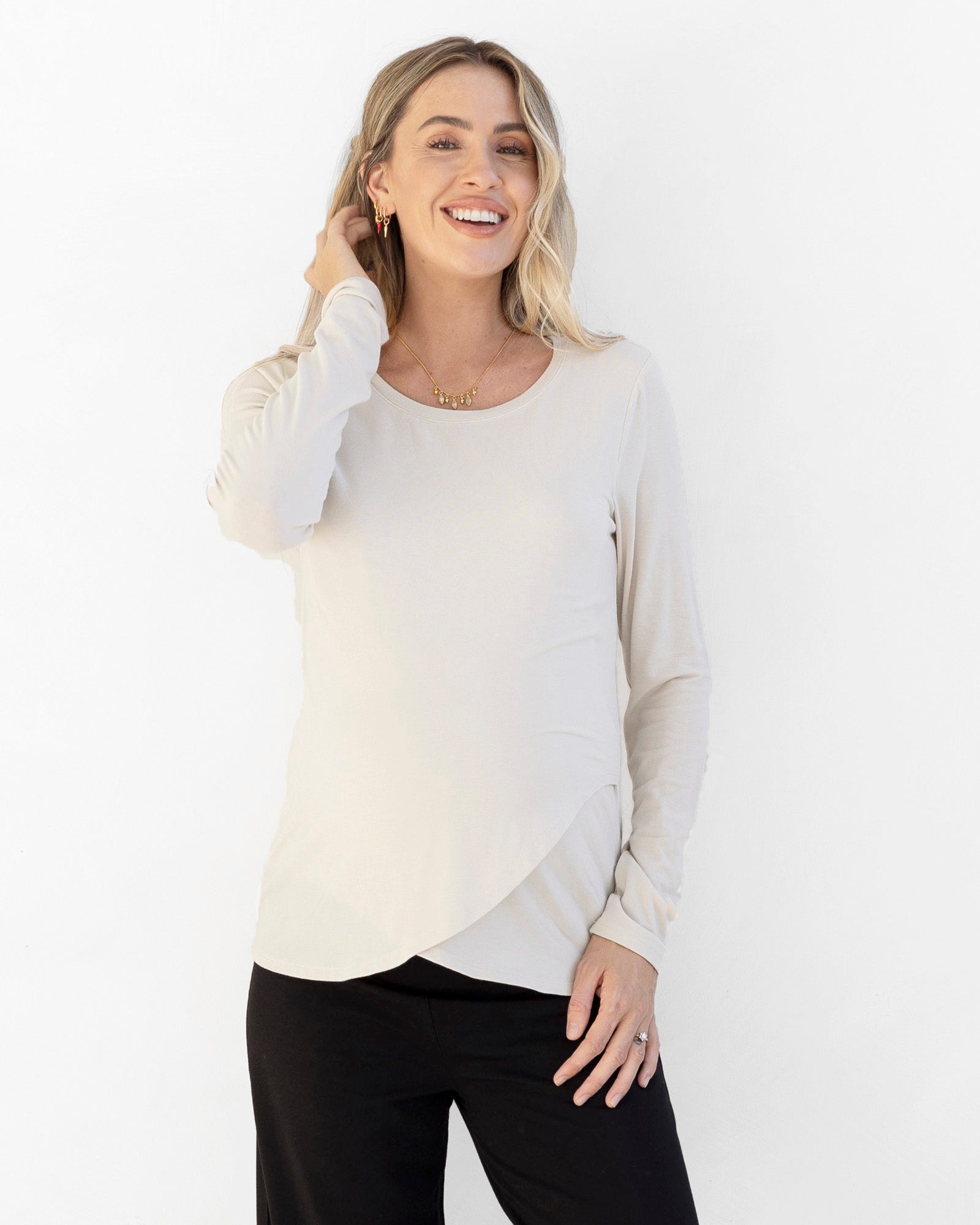 A pregnant lady wearing a long sleeve maternity nursing top in white, with a round neckline and a layering design that provides nursing access.