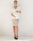Pregnant woman wearing a white top and beige maternity work skirt against a white background