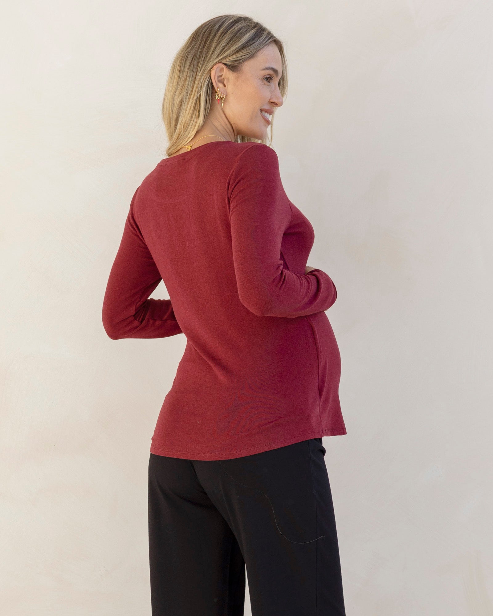 Woman wearing a red nursing sweater and black pants against a plain background