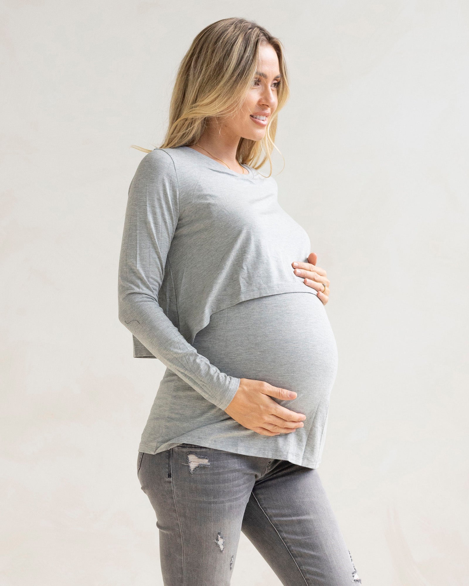 Pregnant woman wearing a gray long-sleeve  maternity top and black maternity jeans background