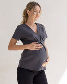 Pregnant Woman wearing a dark grey maternity top and black pants.
