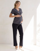 Pregnant woman in dark gray top and black pants standing indoors.