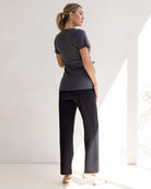 Woman in dark gray top and maternity high waist black pants standing indoors
