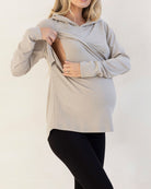 Woman wearing a light gray hoodie with a baby carrier, standing against a white background