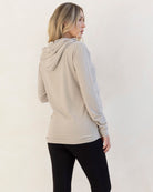 Woman wearing a beige nursing hoodie and black pants against a white background