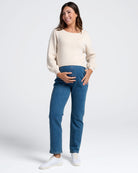Woman wearing a cream sweater and blue maternity jeans