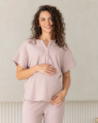 Woman wearing a light pink maternity lounge top and maternity shorts outfit with a plain background
