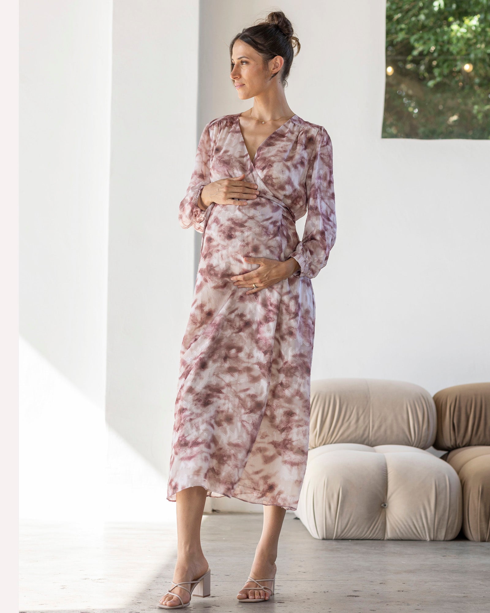 Woman in a floral maternity dress standing in a modern living room.