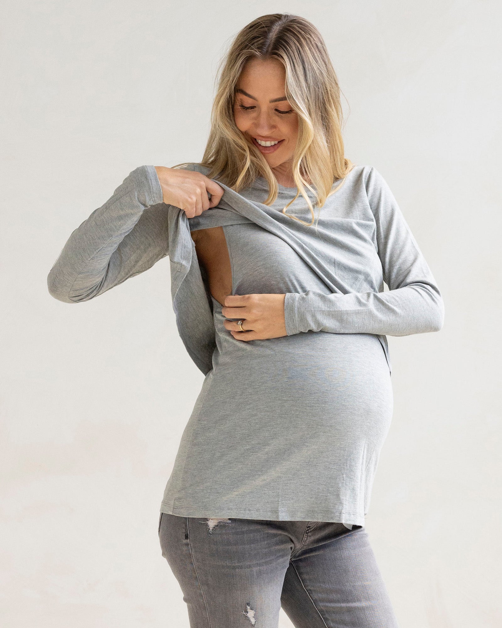 Woman wearing a gray long-sleeve breastfeeding top and gray maternity  jeans against a white background