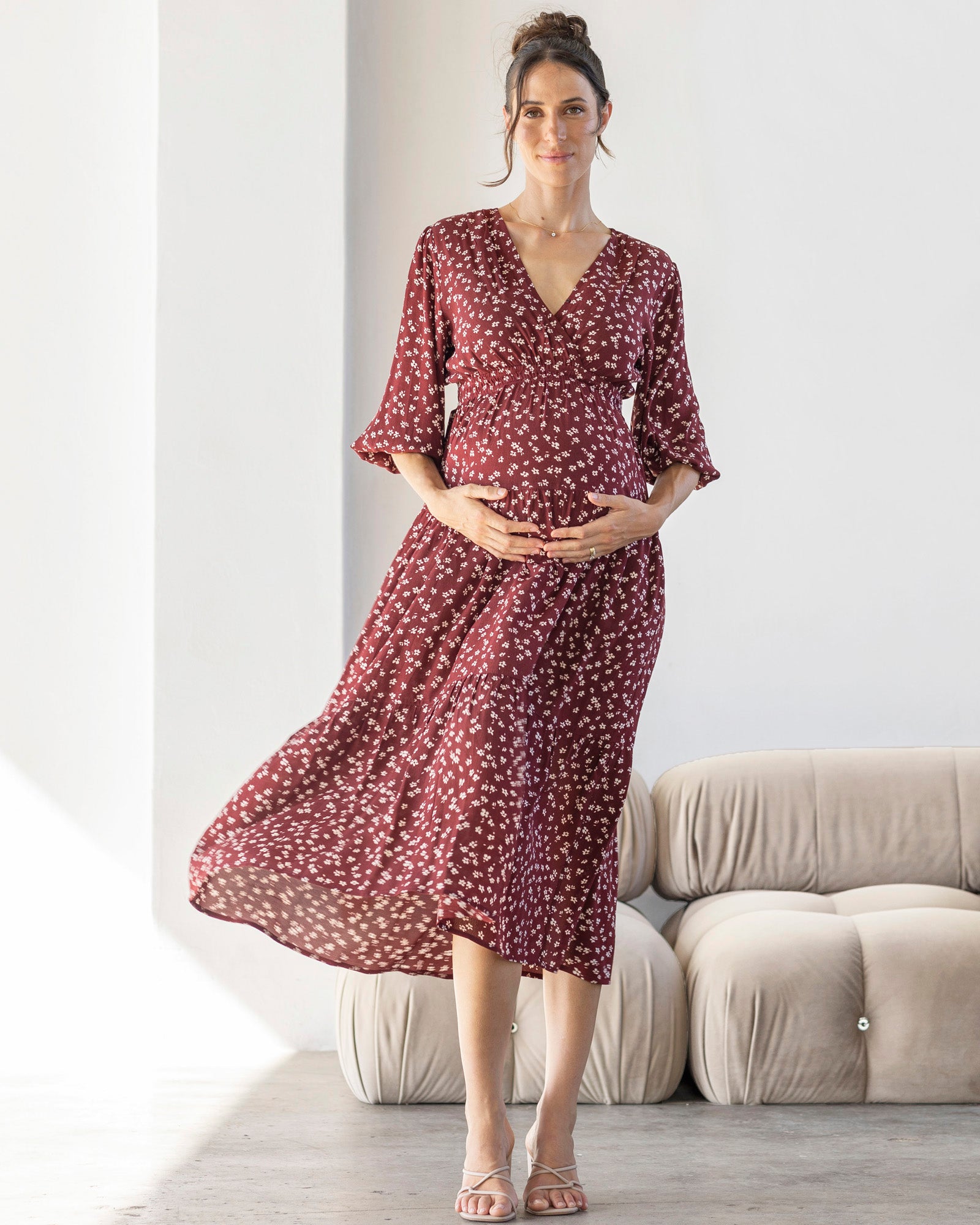 A pregnant woman wearing a burgundy floral maternity maxi dress with a flattering crossover V-neckline and 3/4 puff sleeves. The dress has an elasticized waistband and a flowing tiered skirt.