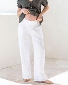 Pregnant woman wearing a green top and white linen maternity pants