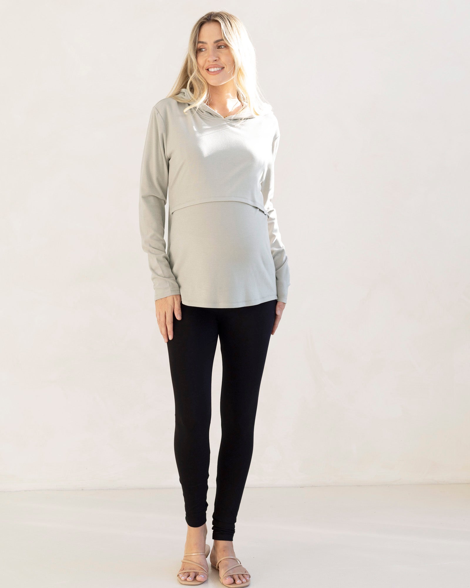 Woman wearing a light gray hoodie and black leggings against a white background