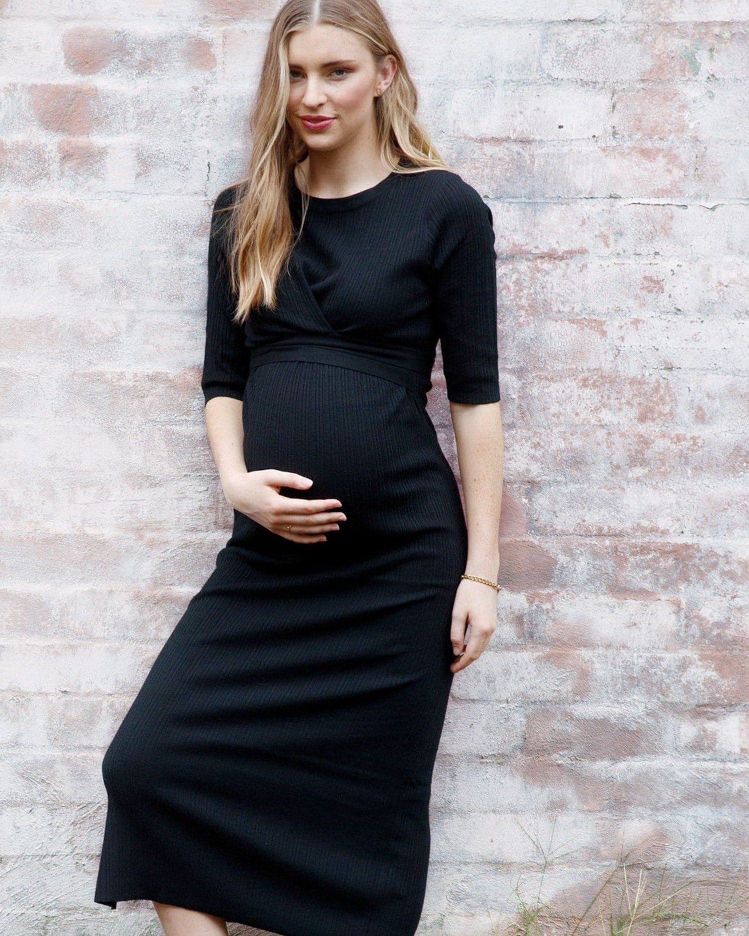 A woman in black angel maternity annabella knit dress against the wall, front (6594399666279)