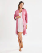 Woman wearing a pink robe over a striped nightgown on a white background