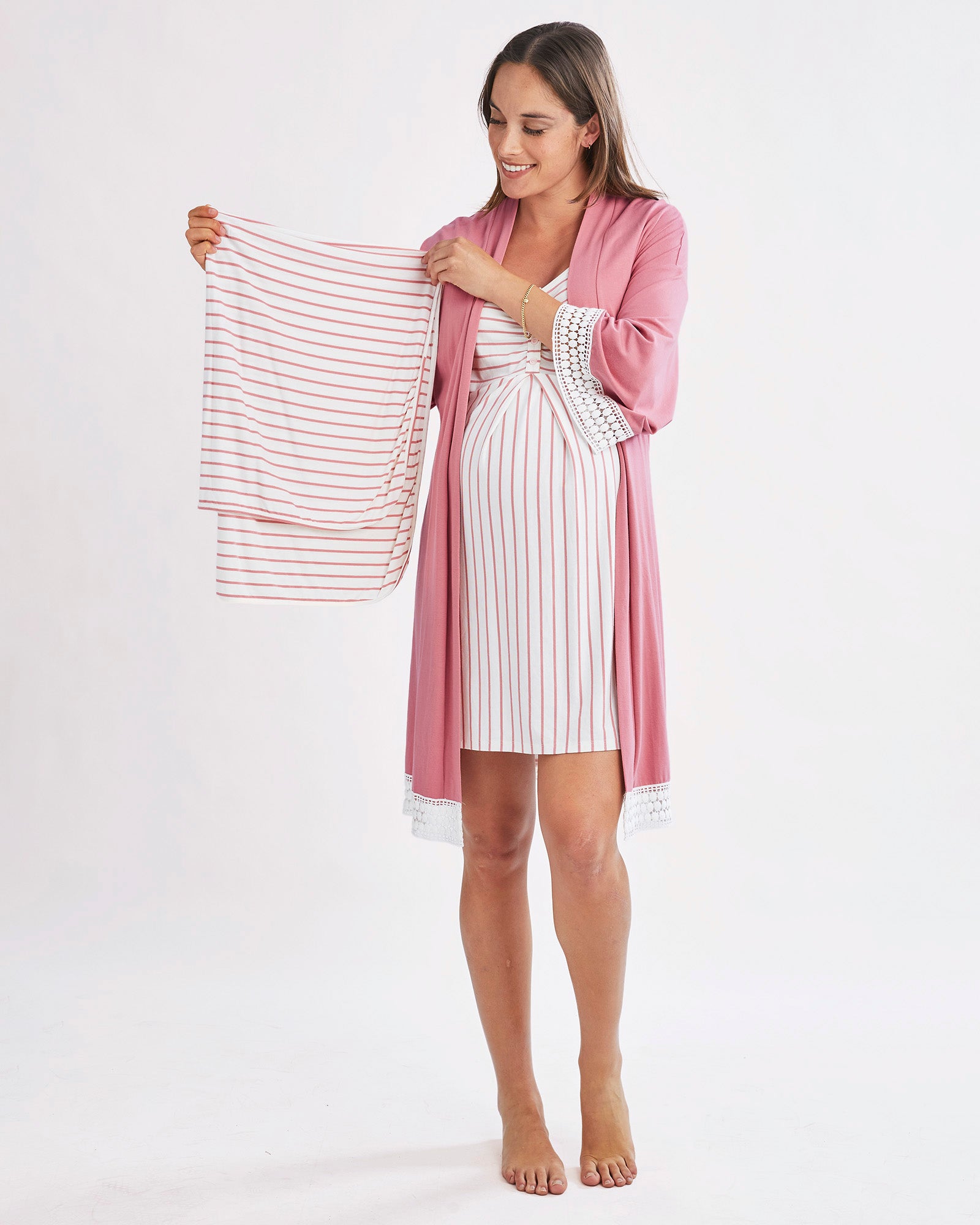 Woman holding a striped baby blanket wearing a pink robe and white dress on a white background