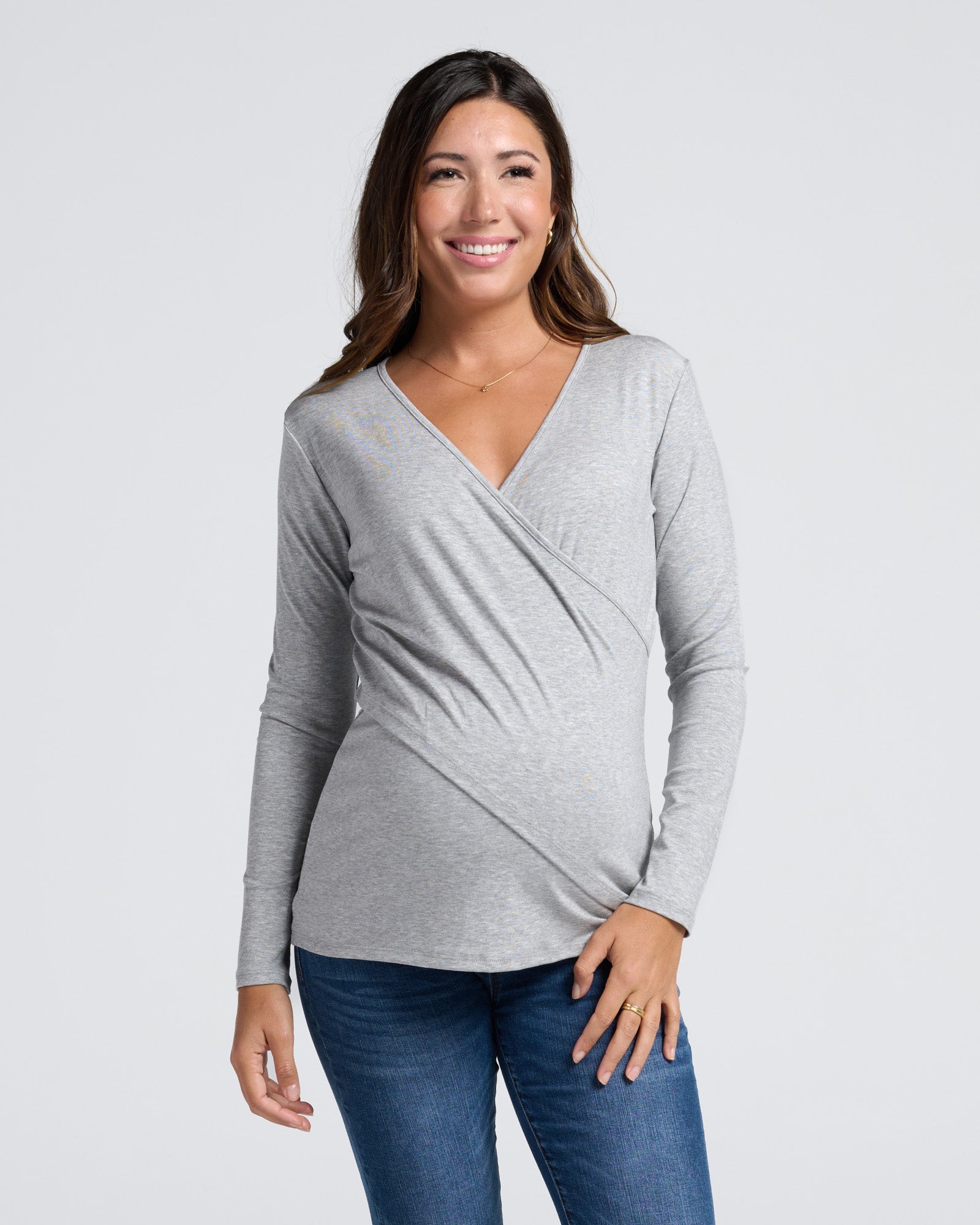 Woman wearing a gray long-sleeve maternity essential layer top, with front cross panel, easy for breastfeeding and blue maternity jeans 