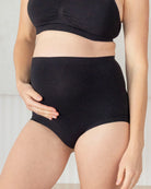 Person wearing black high-waisted underwear and a black crop top against a neutral background