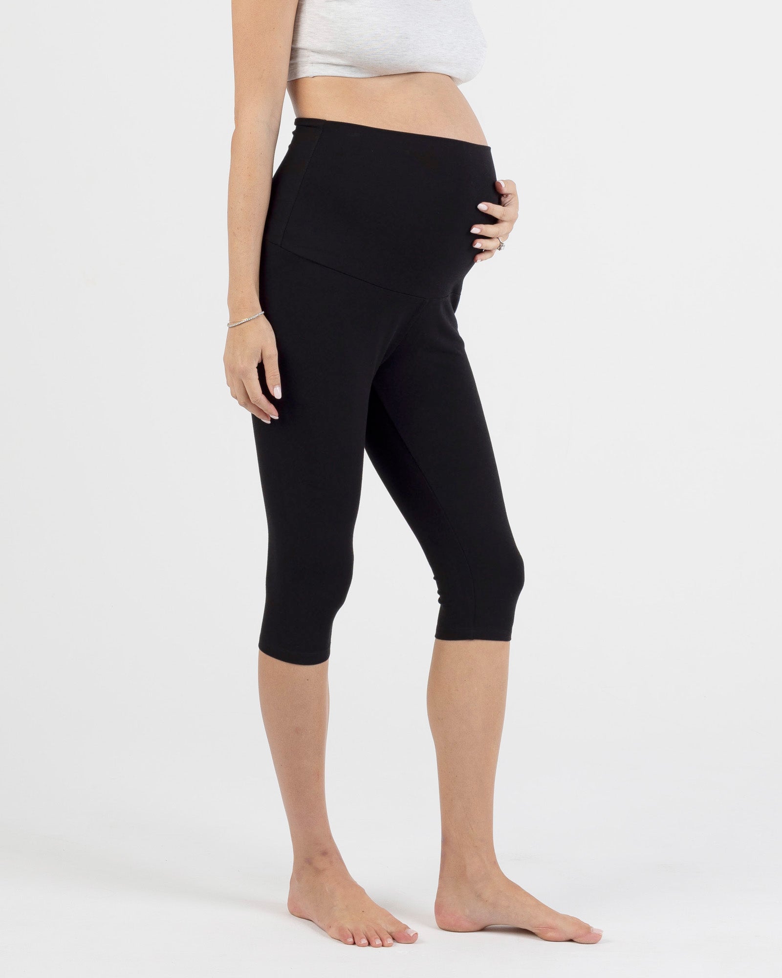 Person wearing black capri maternity leggings on a white background