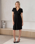 Woman wearing a black dress standing in a minimalistic room.