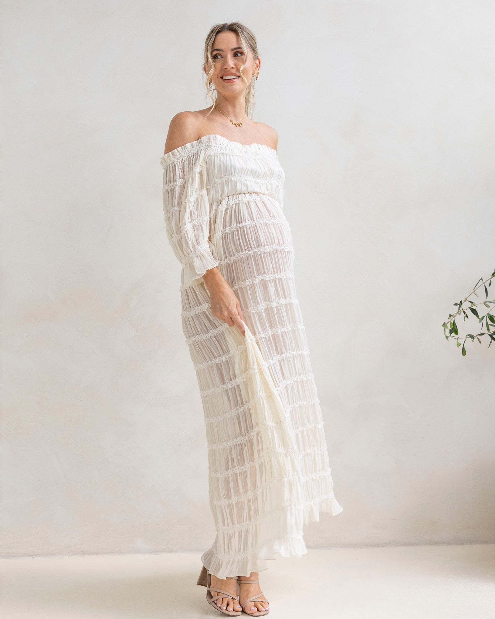Woman wearing a white off-shoulder maternity dress at home in baby shower event