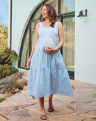 Front view- A Smiling pregnant woman wearing tiered blue striped maxi dress from Angel Maternity