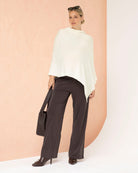 Woman wearing a white poncho and dark pants against a peach background