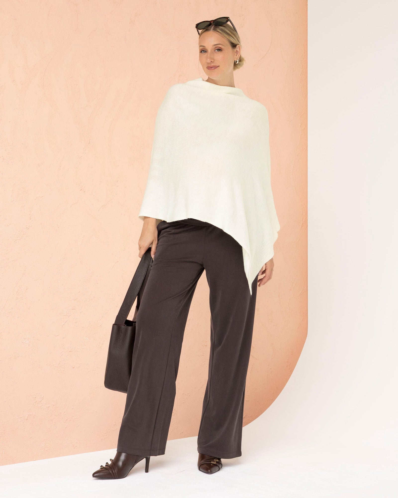 Woman wearing a white poncho and dark pants against a peach background