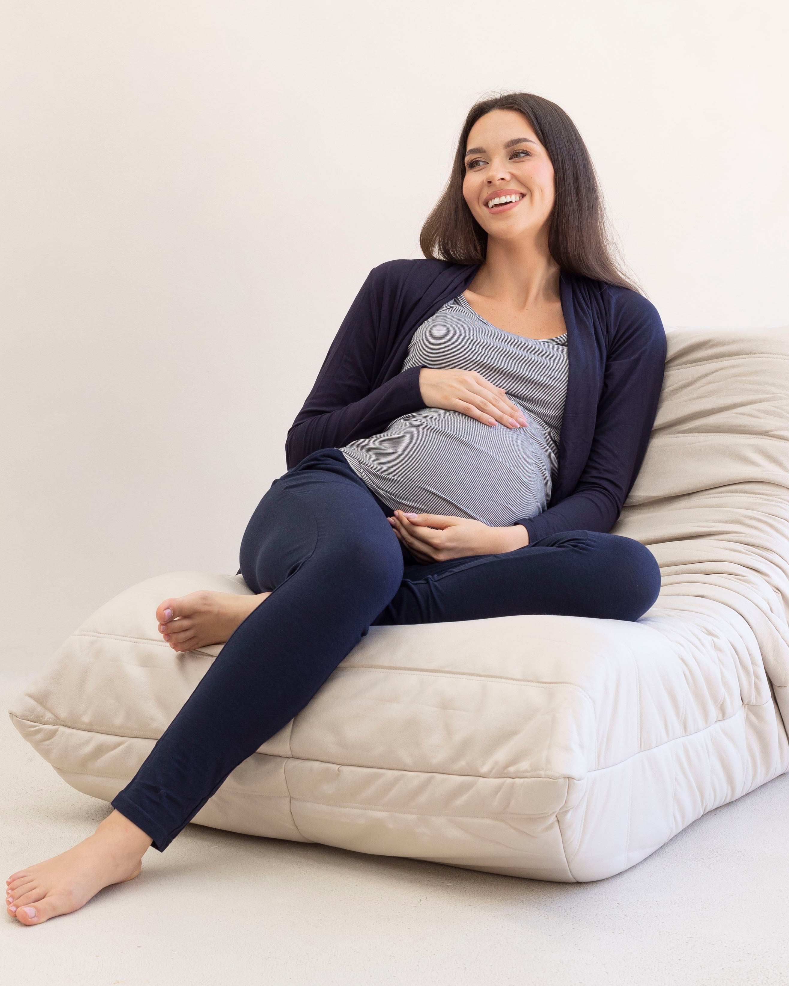 Pregnant woman sitting on a bean bag chair wearing a navy cardigan and leggings.