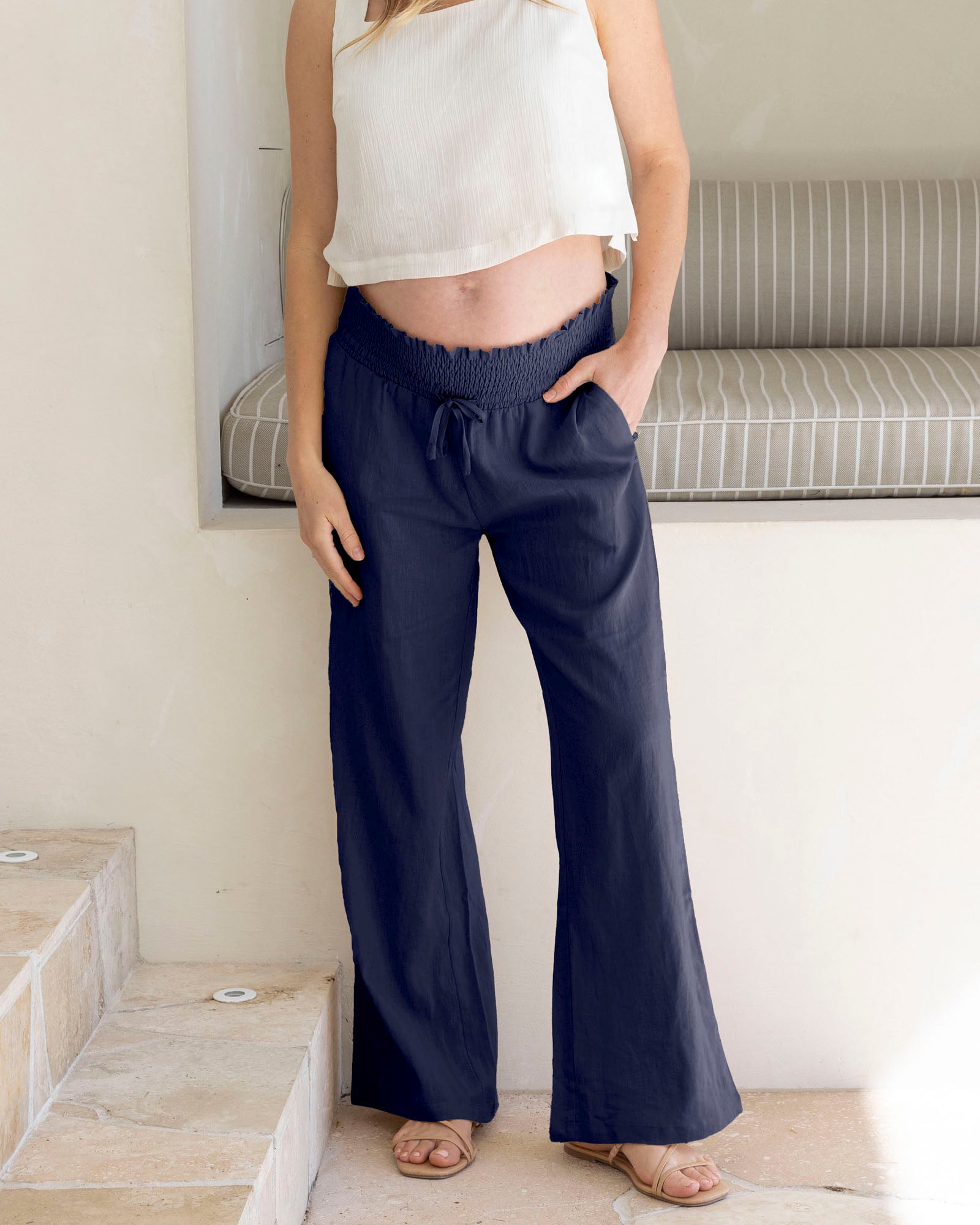 pregnant lady wearing navy wide-leg maternity linen pants and a white top in a minimal indoor setting.