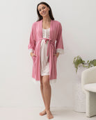 Woman wearing a pink robe and striped nightgown in a minimalistic room.