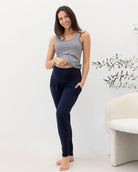 Woman wearing a gray tank top and navy pants standing in a minimalistic room with a plant.