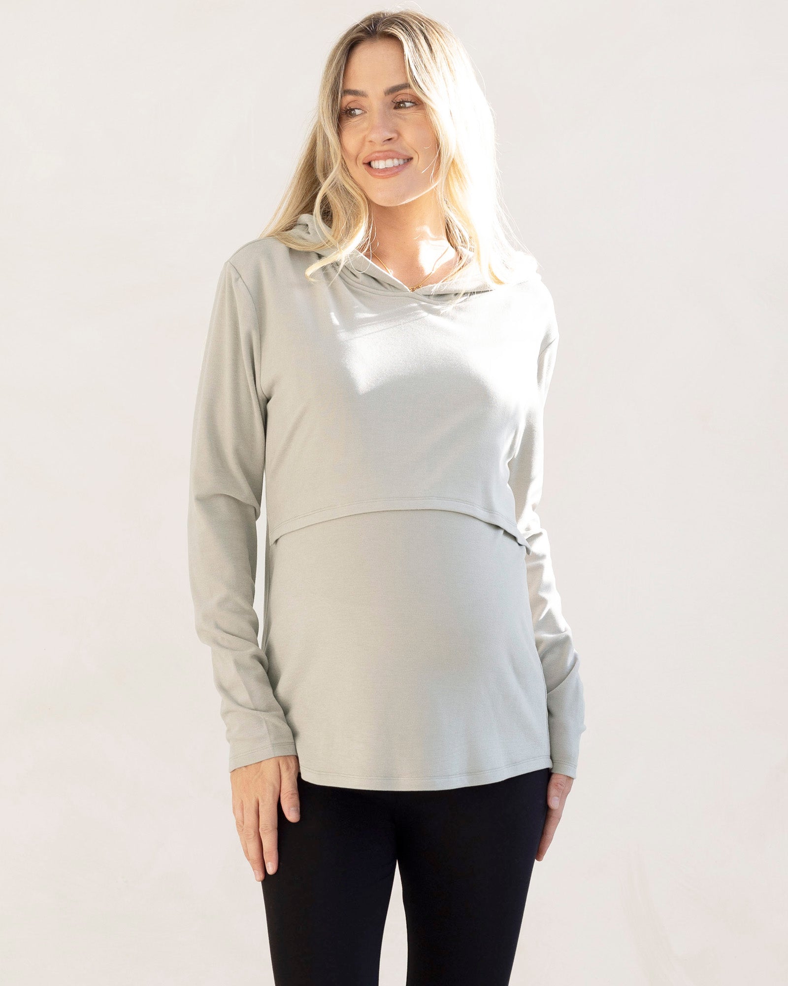 Woman wearing a light gray maternity  hoodie with nursing panel  and black maternity leggings 